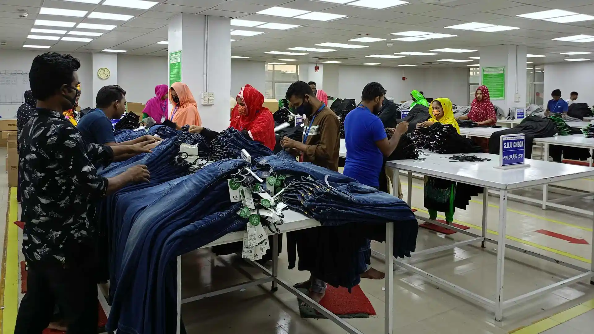 Factory workers at Pioneer Group carefully inspecting and organizing denim pants in the finishing section before shipment.