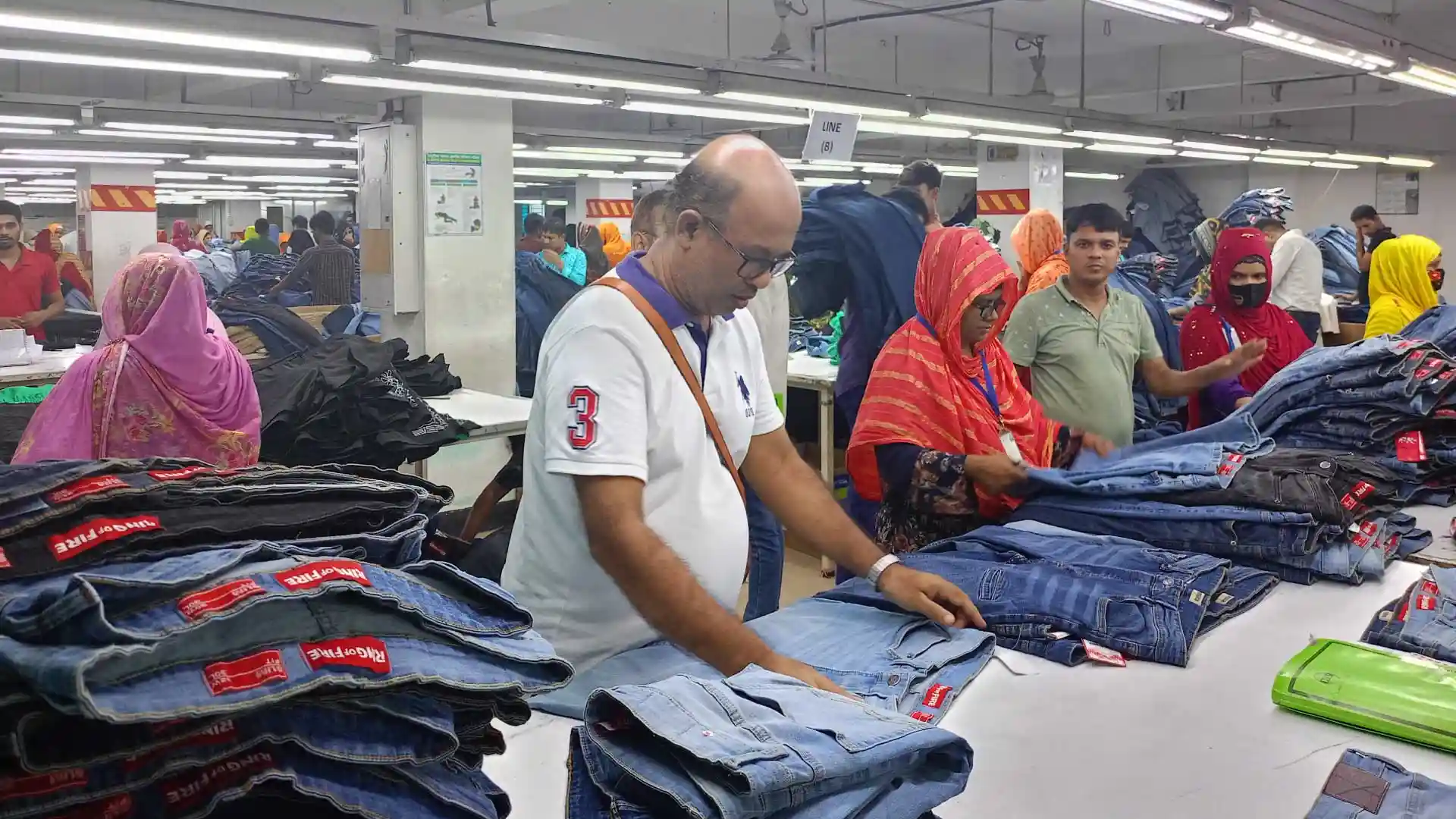 RYZEAL Sourcing team overseeing denim production at a factory, carefully inspecting stacks of jeans for quality assurance alongside factory workers.