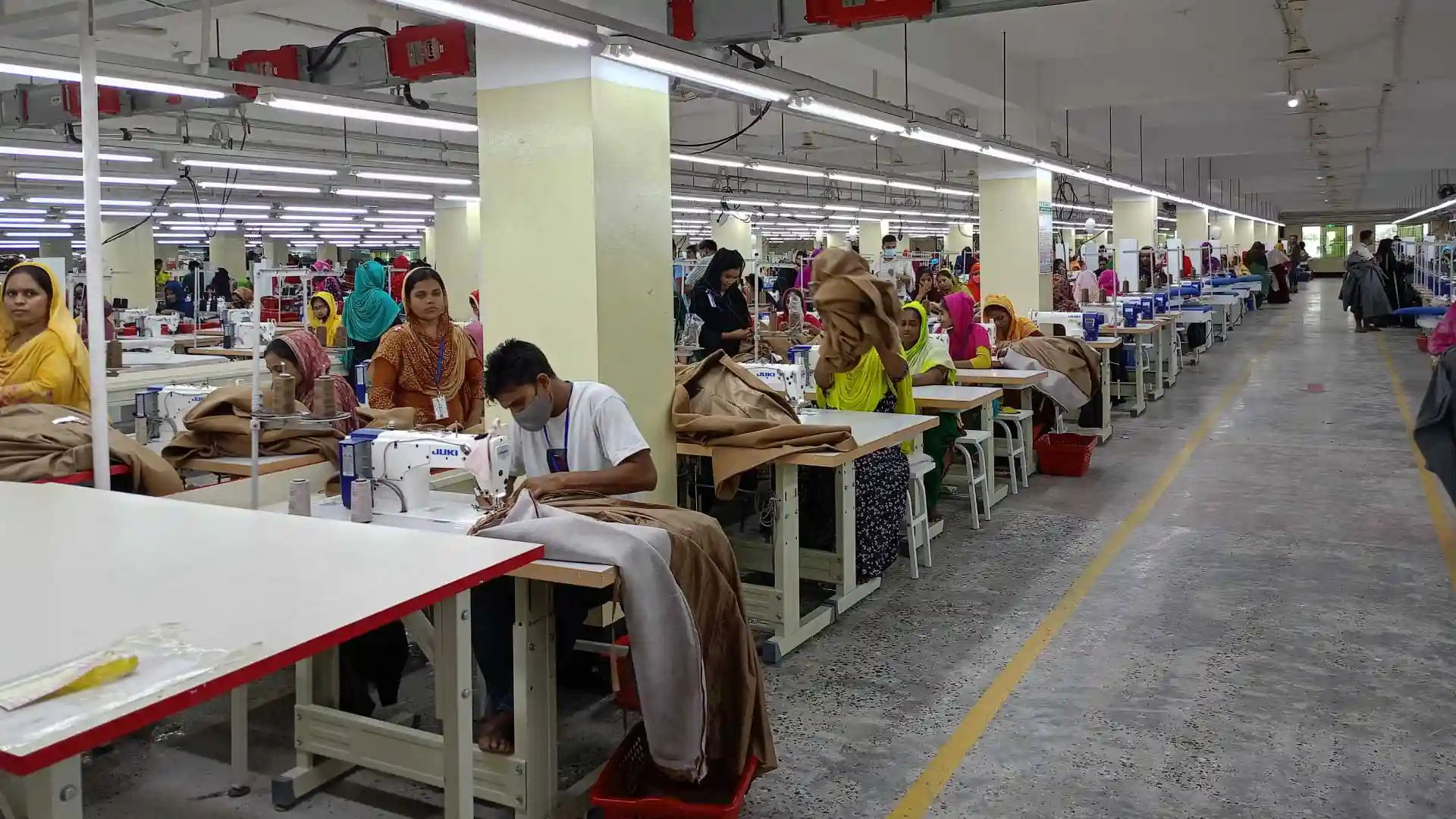 Outerwear factory sewing section with workers stitching garments at industrial sewing machines.
