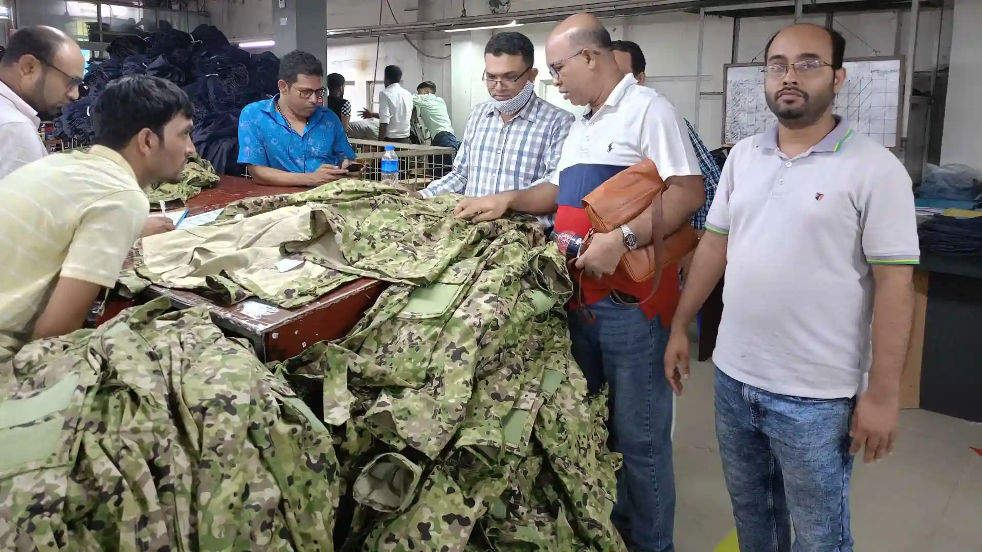 RYZEAL SOURCING team inspecting camouflage workwear garments in a factory.
